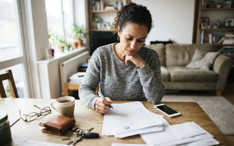 A homeowner reviewing a home insurance policy document at a table, with a damaged door lock visible in the background
